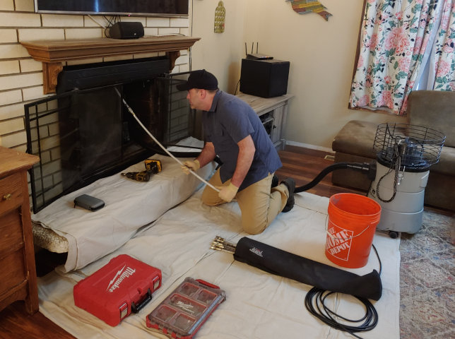 A chimney sweep in front of a fireplace with chimney cleaning tools sitting on a white drop cloth