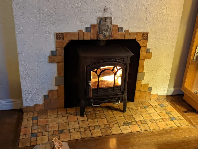 A fire burning inside a quaint wood stove which has been installed inside a 1900's fireplace with original beautiful tilework