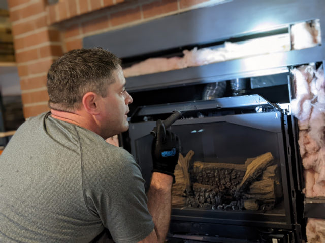 A chimney technician examining a partially disassembled fireplace with a flashlight