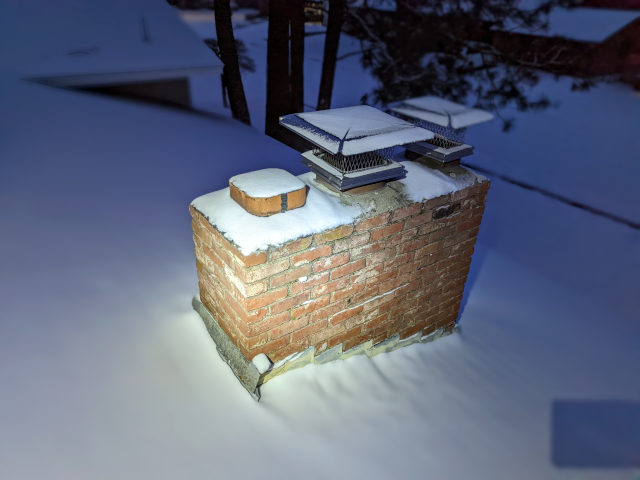 A chimney in the middle of a snowy roof at night